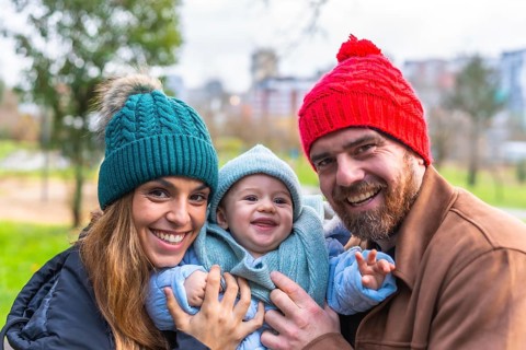 Smiling parents holding their baby wearing winter clothes and wool hats, enjoying a sunny winter
