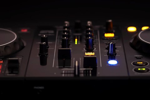 A black DJ mixer with various buttons and knobs, illuminated against a dark background, creating a