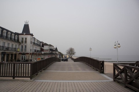 Overcast day on a boardwalk with people walking near waterfront buildings and street lamps, Mielno,