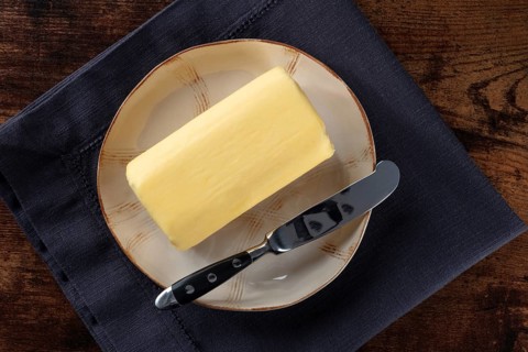 A block of butter with a knife on a plate, overhead flat lay shot on a dark rustic wooden table