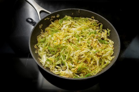 Savoy cabbage in a frying pan on the black stove, cooking at home with healthy winter vegetables,
