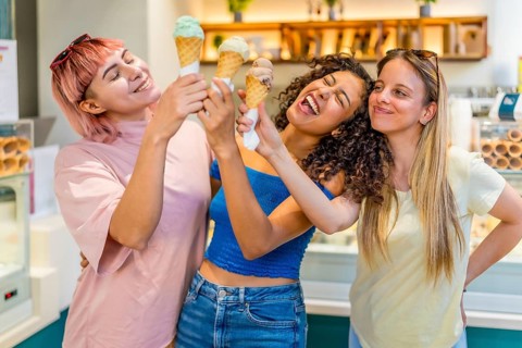 Funny diverse female friends toasting with ice cream cones in store