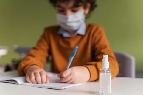 Front view child with medical mask class with bottle hand sanitizer desk