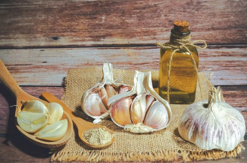 Whole, powdered and chopped garlic on a burlap cloth with a glass bottle with olive oil on a wooden