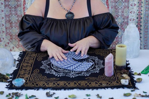 Hands of an unrecognizable fortune-teller woman dressed in black sitting at her table reading tarot
