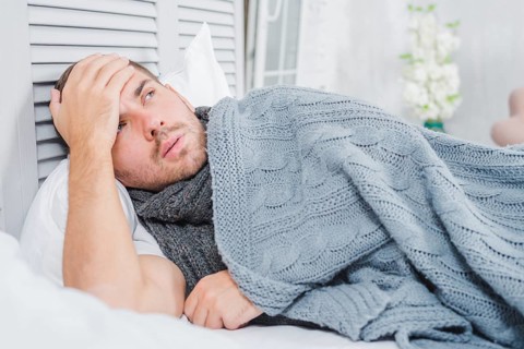 Young man lying bed with headache fever touching his forehead