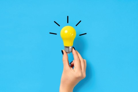 Female hand hold yellow light bulb on blue background. Creative idea, innovation, brainstorming