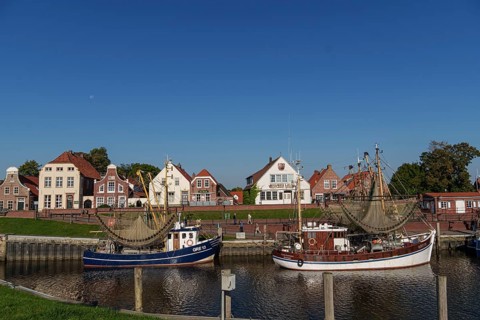A quiet harbour with two boats and picturesque brick houses under a clear blue sky, Greetsiel, East