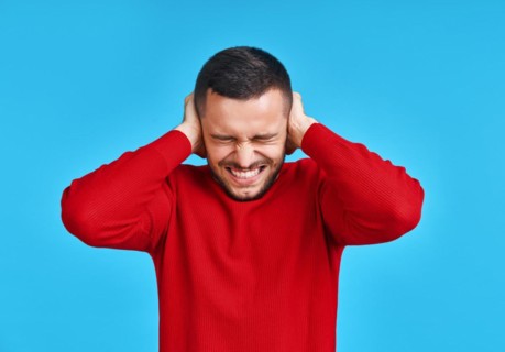 Handsome man covering his ears with hands afraid to hear bad news isolated on blue background.