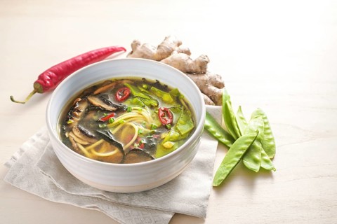 Spicy Asian vegetable soup with noodles, miso, nori seaweed, ginger and chili in a bowl on a wooden