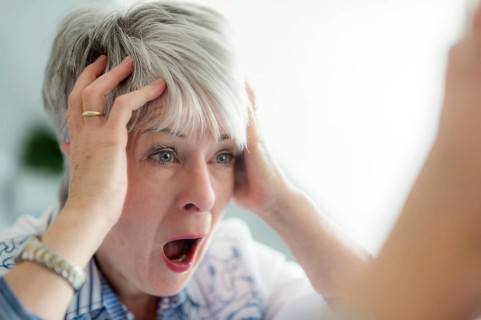 An elderly lady looks in the mirror in horror and ruffles her hair