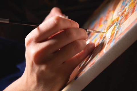 Close-up of a female artist's hand painting with watercolors color on canvas with a brush in a dark