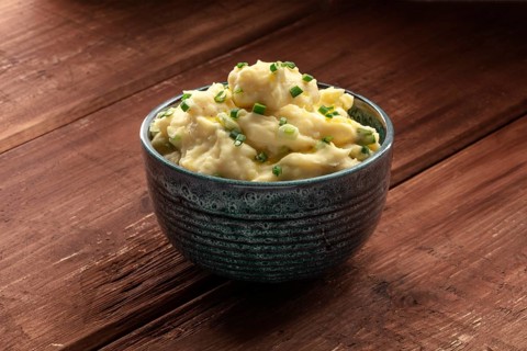 Pomme puree, a photo of a bowl of mashed potatoes with herbs on a dark rustic background with copy