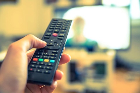 TV remote control in the foreground, tv in the blurry background