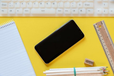 Office desk above view with a black smartphone, white keyboard, and office props