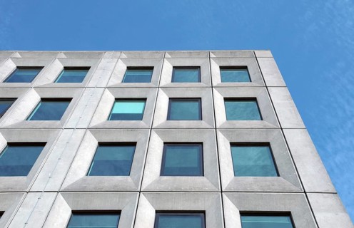 Perspective view of a white concrete office building against a bright blue sky with geometric