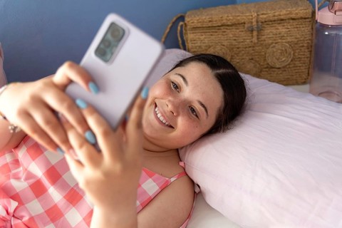 Beautiful and cheerful young Latin American woman in pajamas, taking a selfie with her mobile phone
