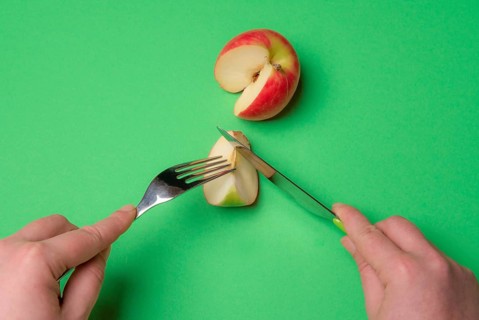 Top view of a woman hands with cutlery, cutting a slice of apple on a green background. Ready to