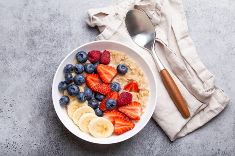 Oatmeal porridge with fruit and berries in bowl with spoon on white wooden background table top