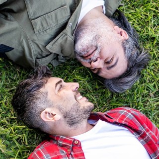Top view of a Hispanic gay couple lying on the grass while looking to each other