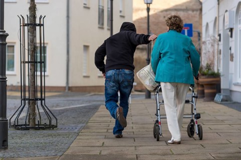 A man snatches a senior citizen's handbag from her shoulder as she passes by. Rear view