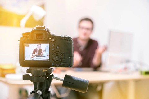 Camera on a tripod filming a blogger at home sitting on his workspace