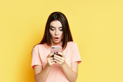 Portrait of a shocked pretty millennial hipster girl using mobile phone isolated over yellow