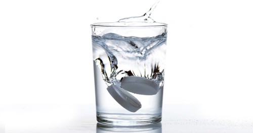Tablets Falling and Dissolving into a Glass of Water against White Background