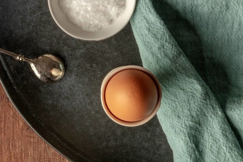 A boiled egg in an eggcup with coarse sea salt and a spoon, shot from above with copy space