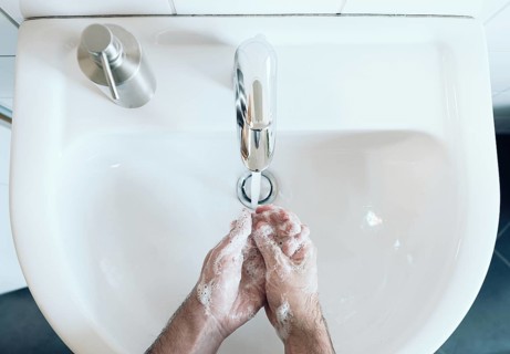 top view of person thoroughly washing hands at bathroom sink with soap and hot water, hygiene