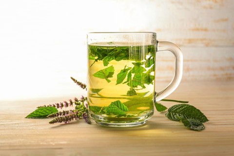 Fresh peppermint leaves brewed as a healthy herbal tea in a glass cup, some flowering stems on a