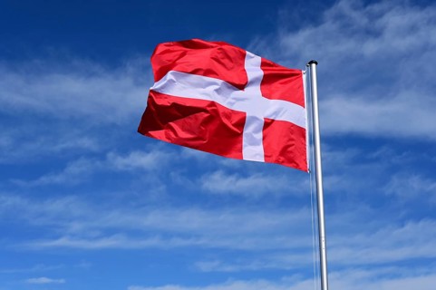 The flag of Denmark flutters in the wind against a blue cloudless sky