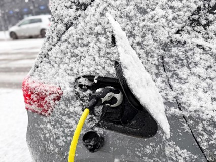 Charging an electric vehicle in winter. A yellow charging cable is connected to the car's charging
