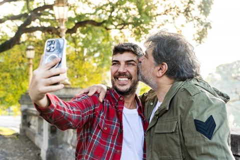 A man is kissing his husband while his husband takes a selfie in that scene