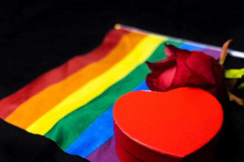 Lgbt wedding concept. Red rose with little heart box on lgbtq rainbow flag on black background