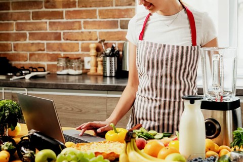 Woman using laptop at home kitchen. Girl touching touchpad with hand, searching for a recipe. Chef