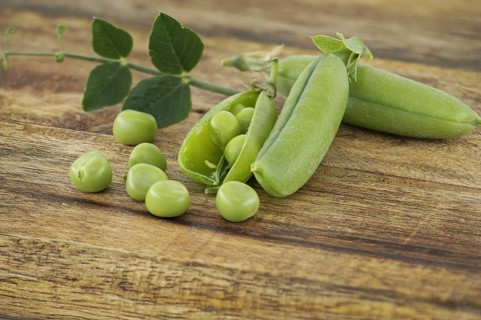 Fresh green peas, pea pods with green leaves and open pea pod on a wooden surface, vegan nutrition