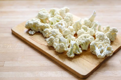 Cauliflower florets on a wooden cutting board, prepared ingredient for cooking a vegetable dish,