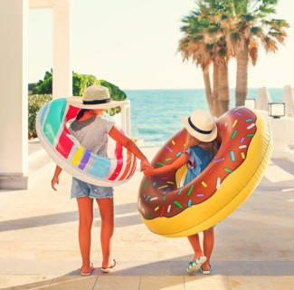 Two small girls with inflatable toys on the beach. Summer vacation and traveling concept