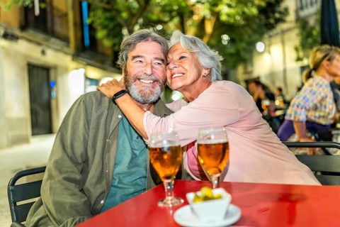 Senior happy couple embracing drinking beer in sidewalk bar in the city