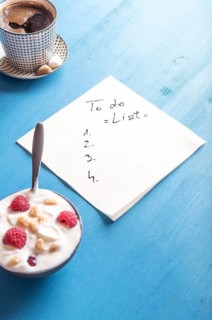 White napkin with a draft of a to do list, surrounded by a bowl of yogurt with cereal and raspberry