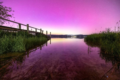 View of a calm lake with pink sky and starry sky with aurora borealis, Reichenau, Lake Constance,