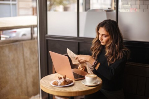 Young businesswoman reading newspaper in cafe in morning, female freelancer drinking coffee and