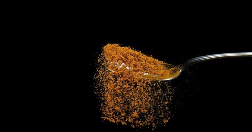 Spoon and Curry Powder falling from Spoon against Black Background