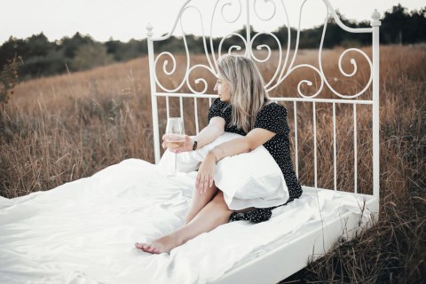 Full body barefoot female with blond hair enjoying wine and looking away while sitting on