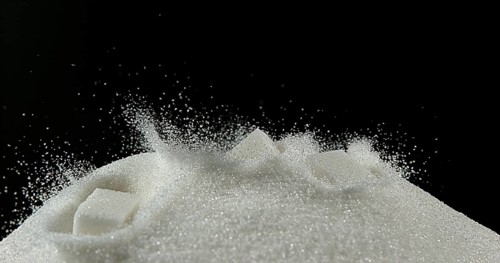 White Sugar Cube falling on Powder Sugar against Black Background
