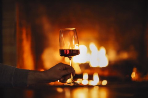Man having red wine by the fireplace. Close up of man holding and drinking red wine glass by open