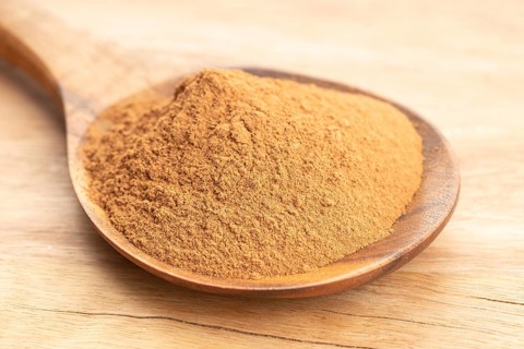 Cinnamon powder in wooden spoon on wooden table. Close up
