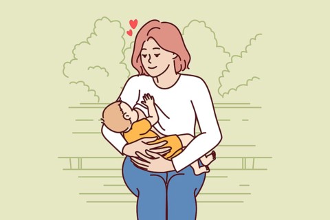 Loving mother breastfeeding baby and looks at baby lovingly sitting on park bench. Caring woman
