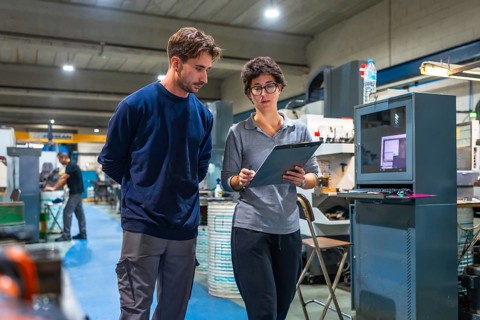 Female manager and male young engineer doing paperwork standing and talking at factory